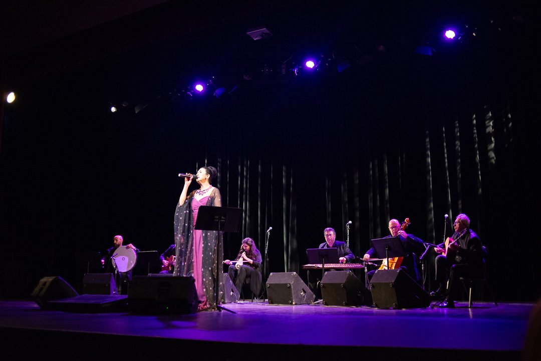 Vocalist and acoustic ensemble under deep blue stage lighting at a theatre concert in Vancouver