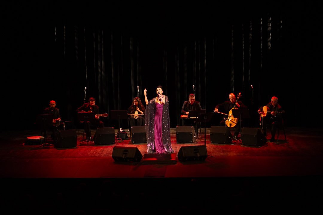 Vocalist with her arms raised mid-song on a red-lit theatre stage