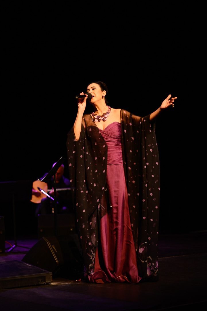 Close frame of the vocalist mid-song in a beaded gown under the stage lights