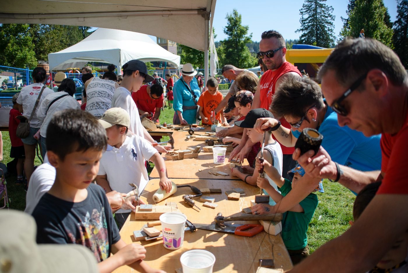 Families side by side at a long table making crafts at a festival activity tent