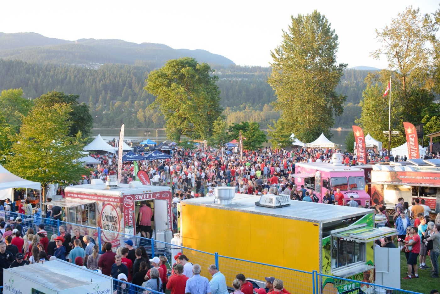 Wide view of the festival grounds packed with visitors, food trucks and vendor tents beside the water