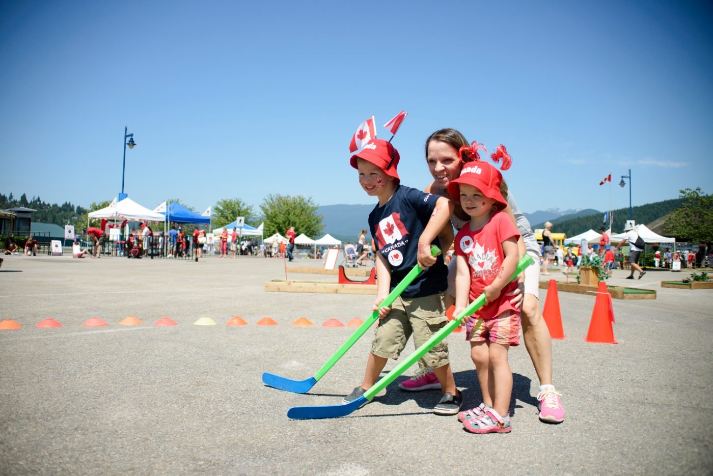 Mother and two children in Canada Day hats playing ball hockey at the festival activity zone