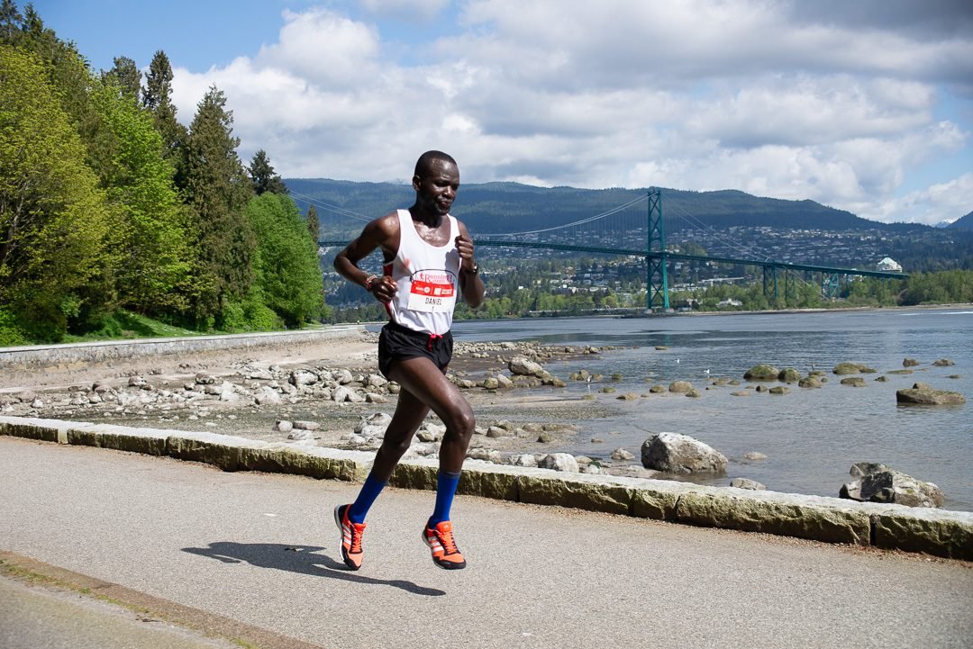 Lead marathon runner on the seawall with the Lions Gate Bridge behind him