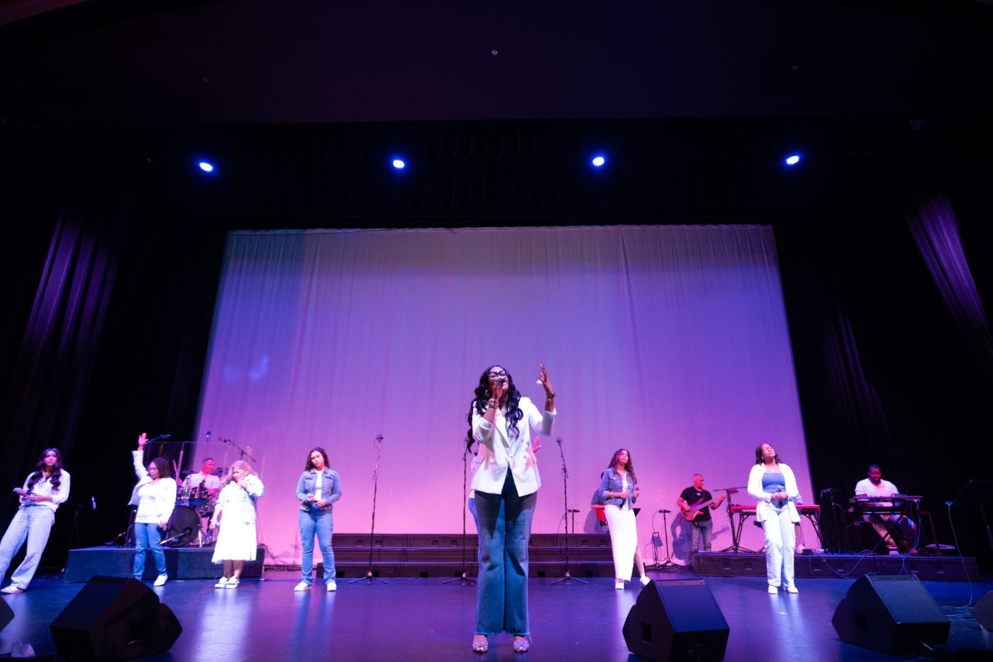 Wide concert photograph of a full band performing under stage lighting in a Vancouver theatre