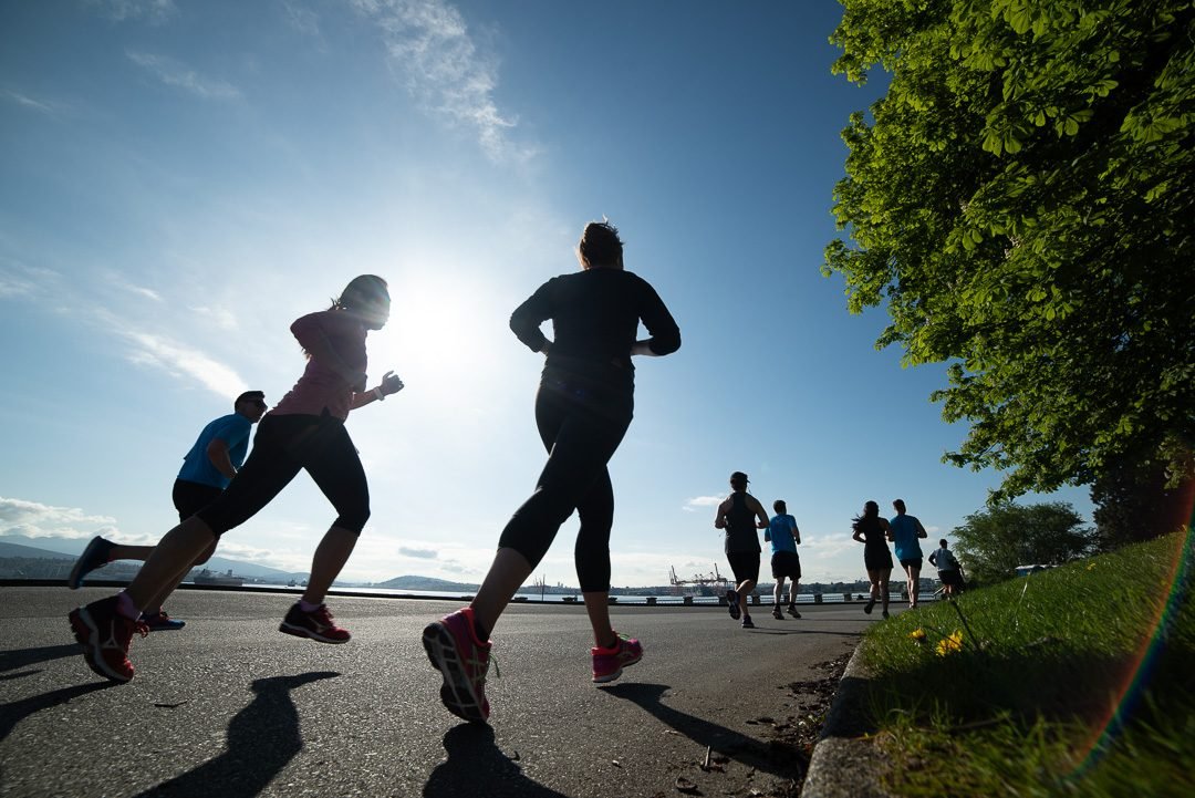 Marathon runners silhouetted against the morning sun on the Vancouver seawall