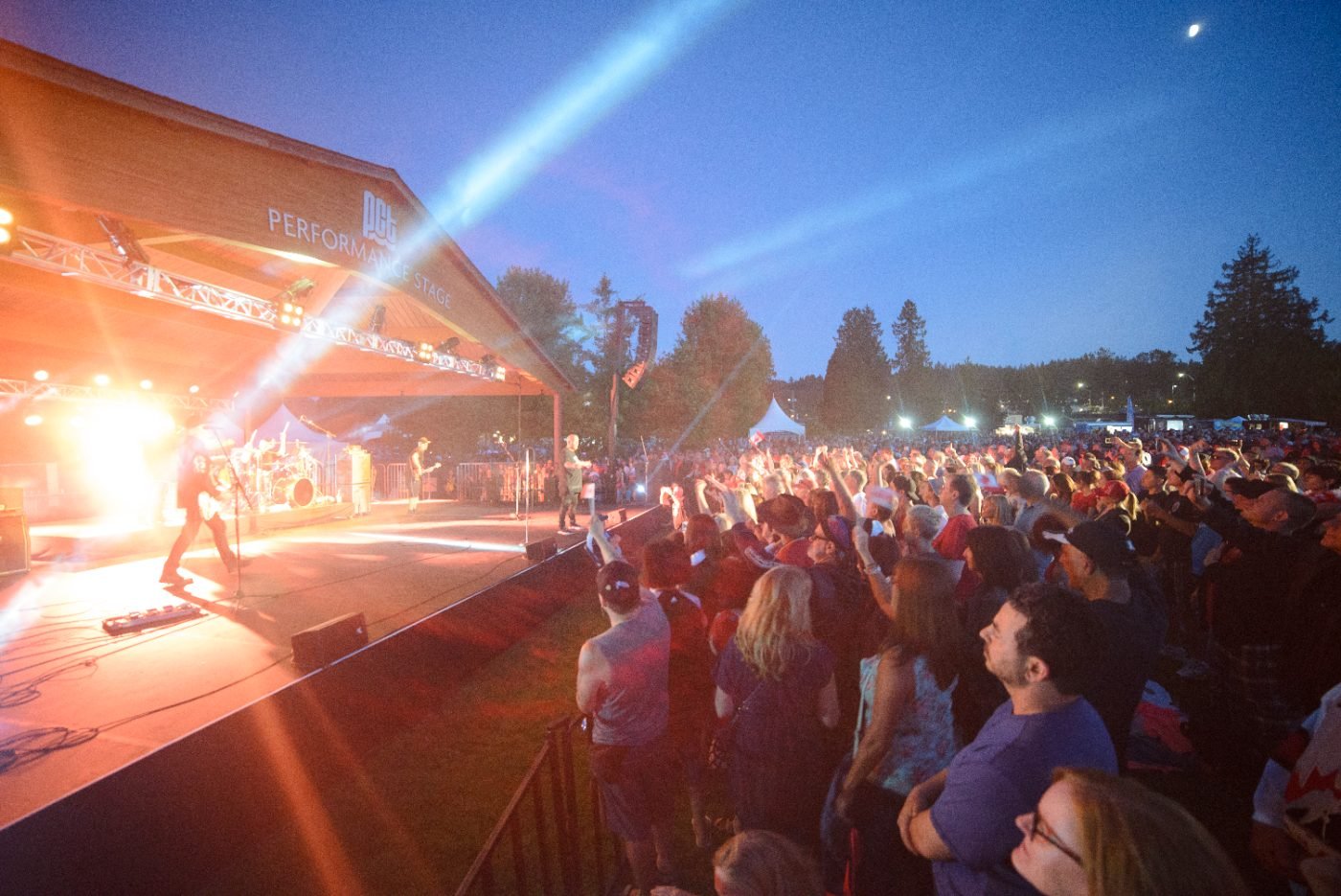 Outdoor concert photographed from the crowd as the stage lights sweep over the audience at night