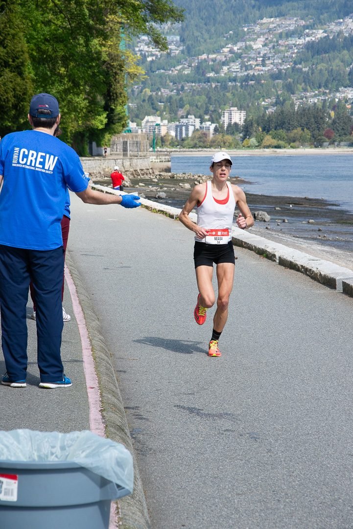 Race volunteer handing a cup of water to a runner at a seawall aid station