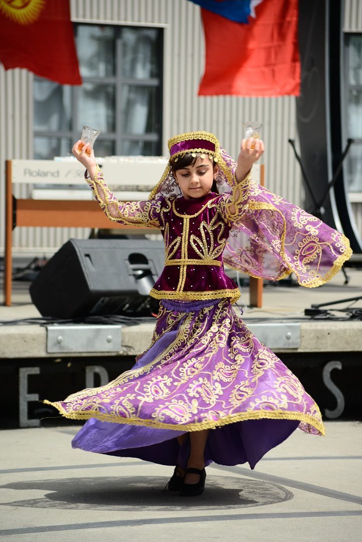 Festival dancer mid-turn in a traditional embroidered costume on an outdoor plaza stage