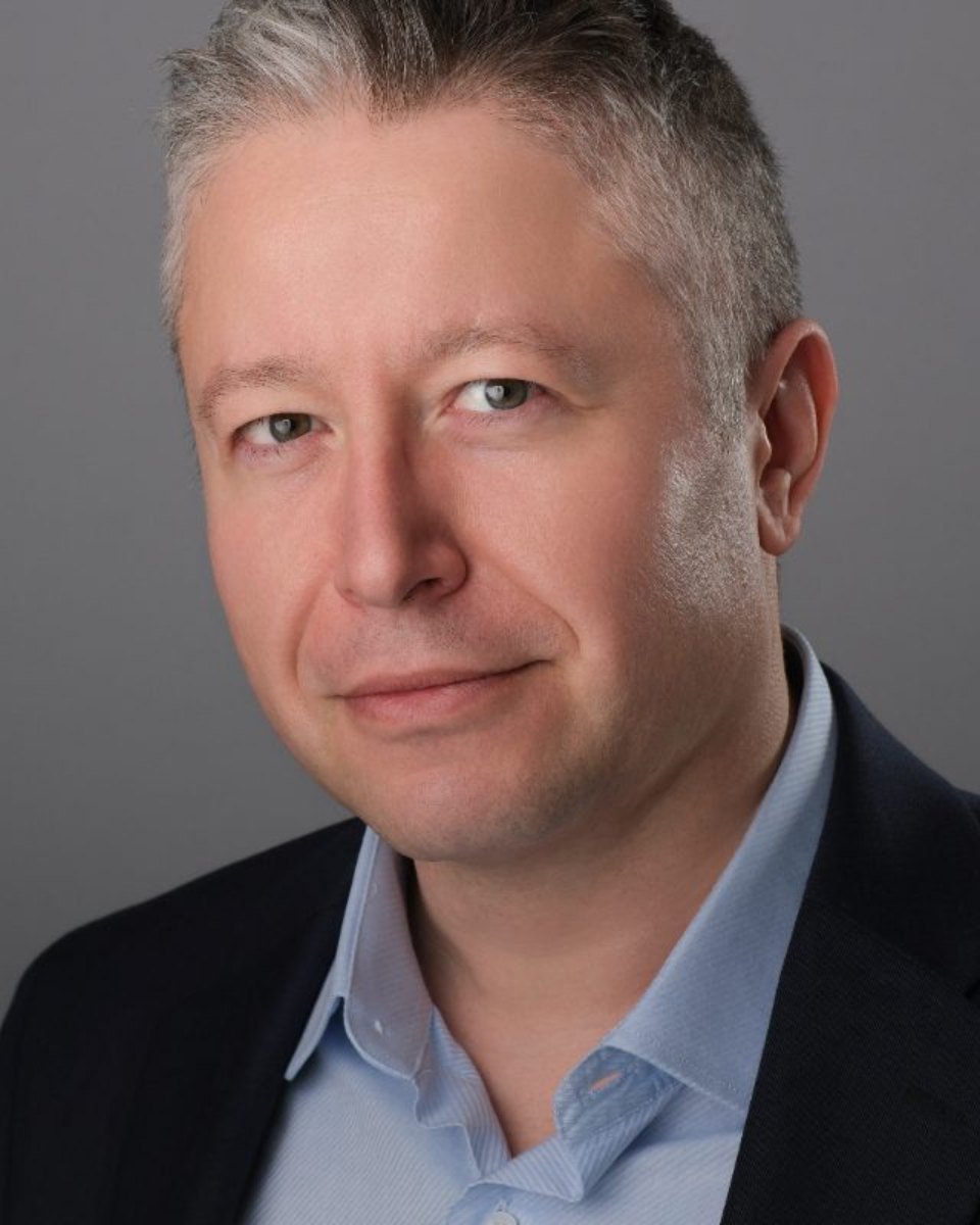 Executive headshot of a man in a dark jacket on a grey studio backdrop