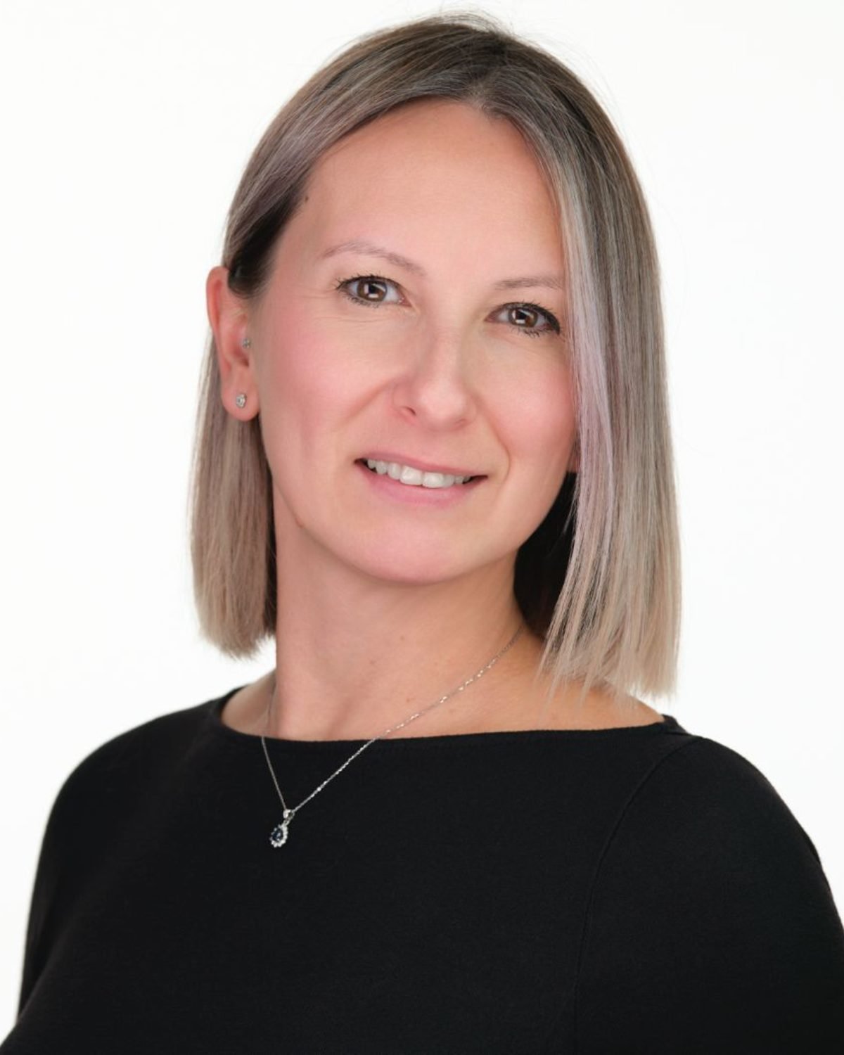 Professional headshot of a smiling woman in a black top on a white background at the Langley studio