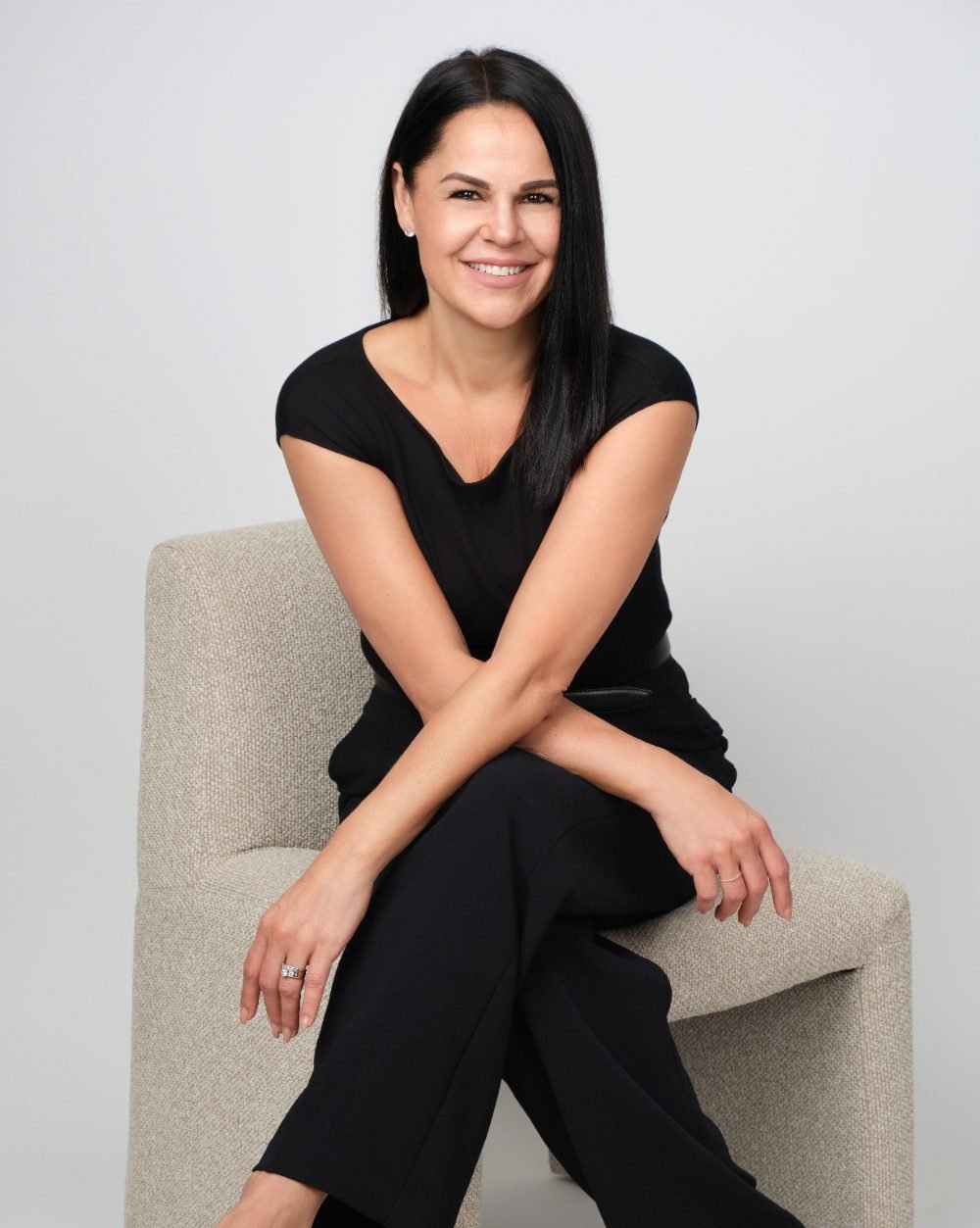 Personal branding portrait of a smiling businesswoman seated in a chair on a light studio backdrop