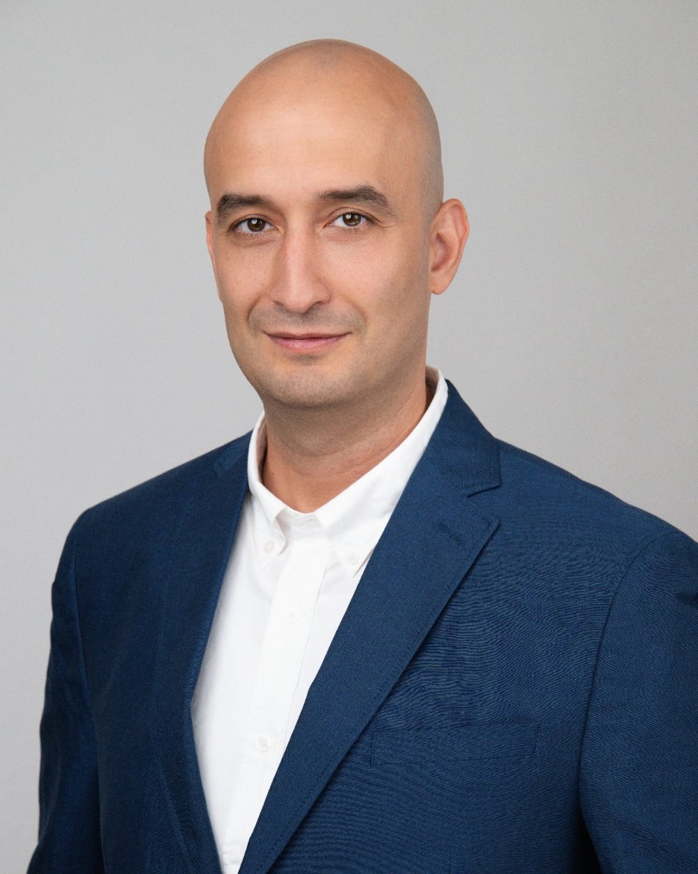 Professional headshot of a man in a navy blazer and white shirt on a grey background