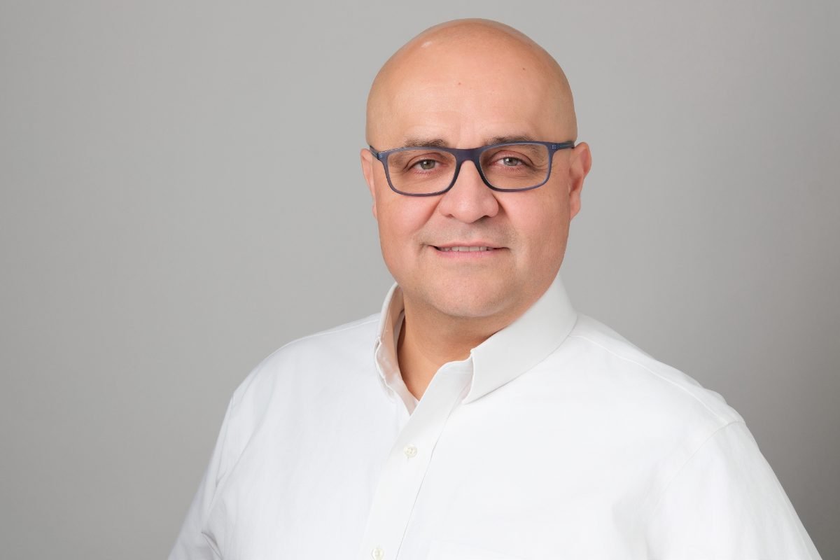 Professional headshot of a man in a white shirt on a grey studio backdrop