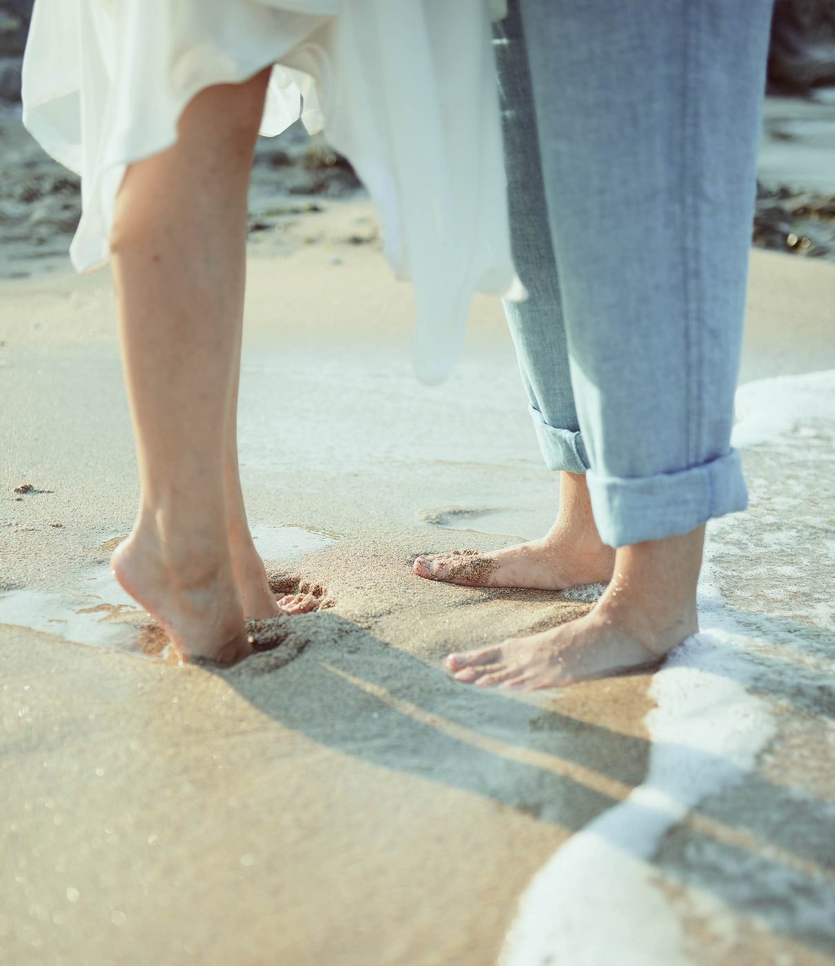 Detail photograph of a barefoot bride and groom standing in the surf after their beach wedding ceremony