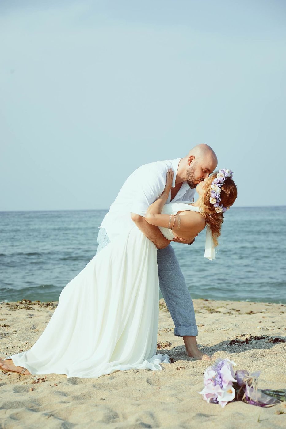 Beach wedding photography of the groom dipping the bride for their first kiss on the sand
