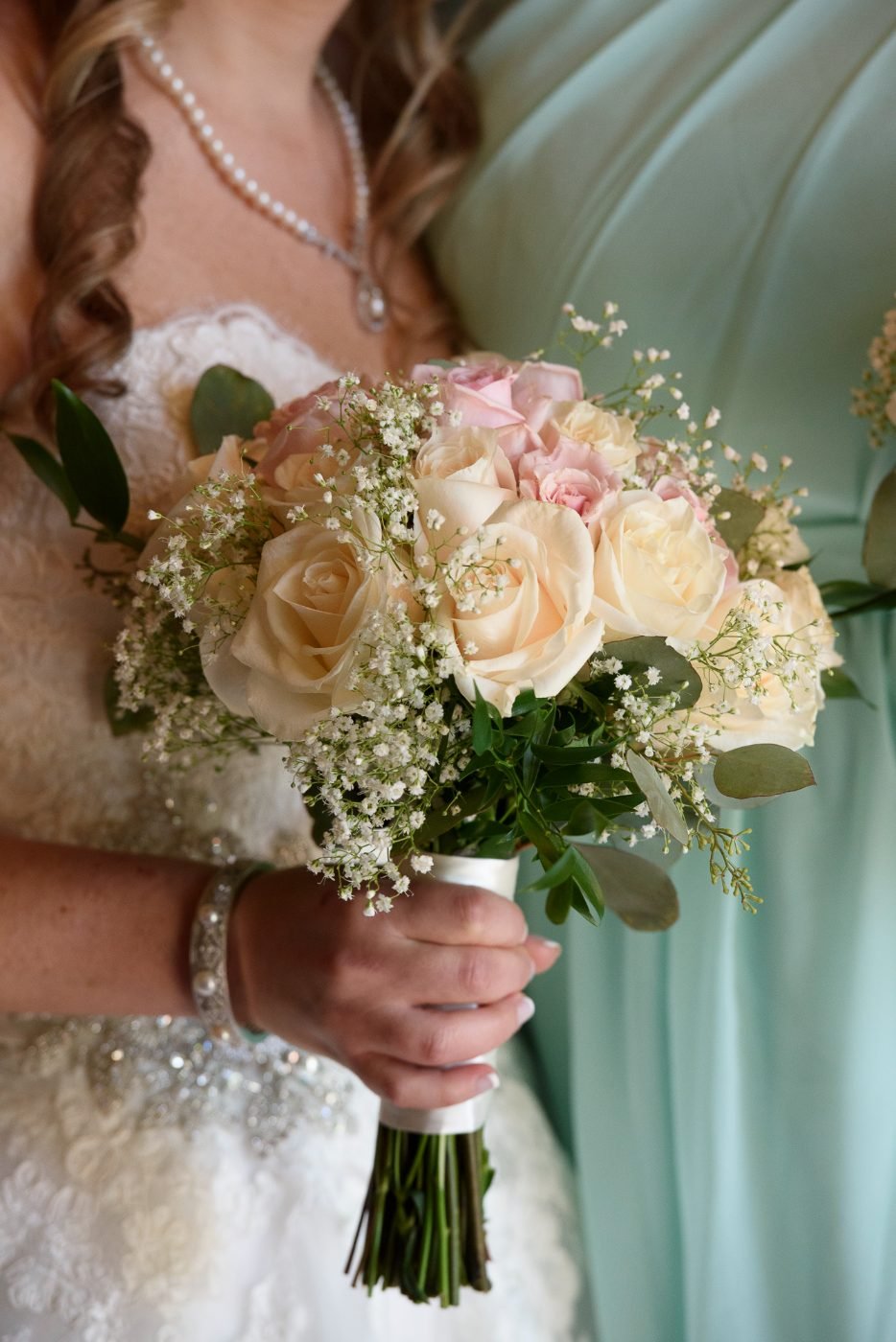 Close up of a bridal bouquet of cream and blush roses with baby&rsquo;s breath held by the bride