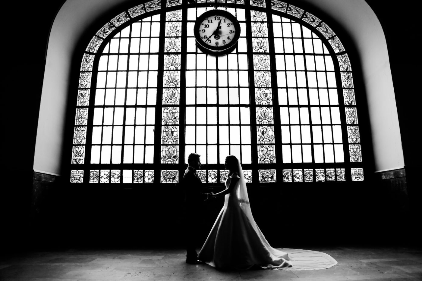 Bride and groom silhouetted against a tall stained glass station window during their wedding portraits