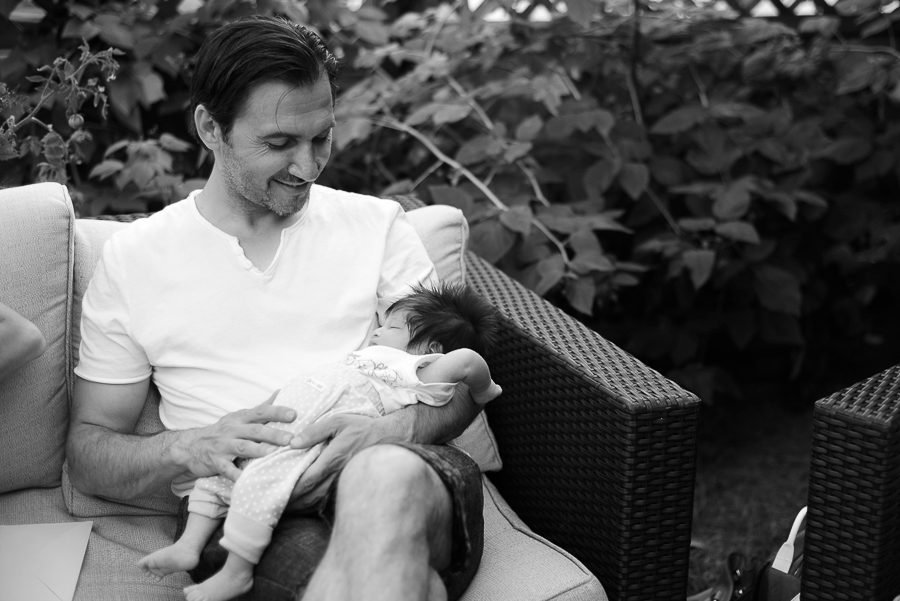 Black and white photograph of a father holding his newborn during a family celebration