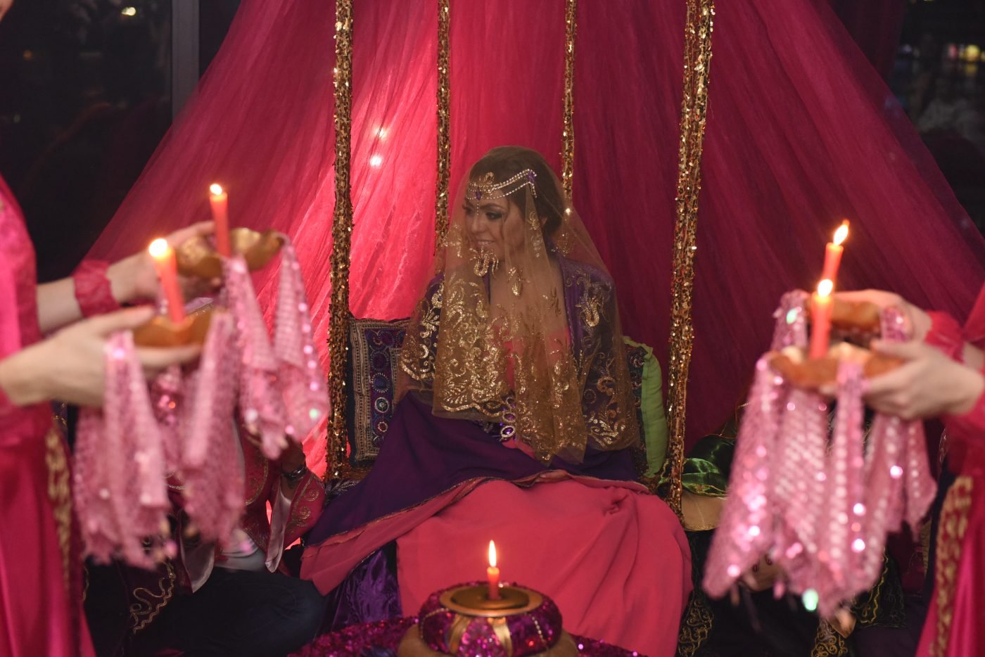 Henna night celebration photography of the bride under a red veil surrounded by candles and traditional dress