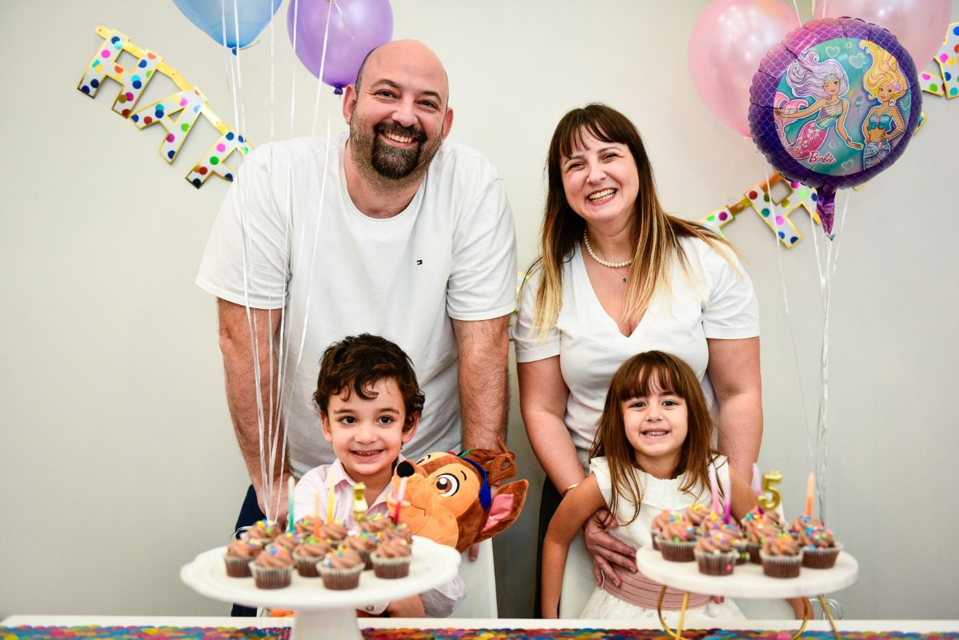 Family photographed behind two cupcake stands at a child&rsquo;s birthday party with balloons in the background