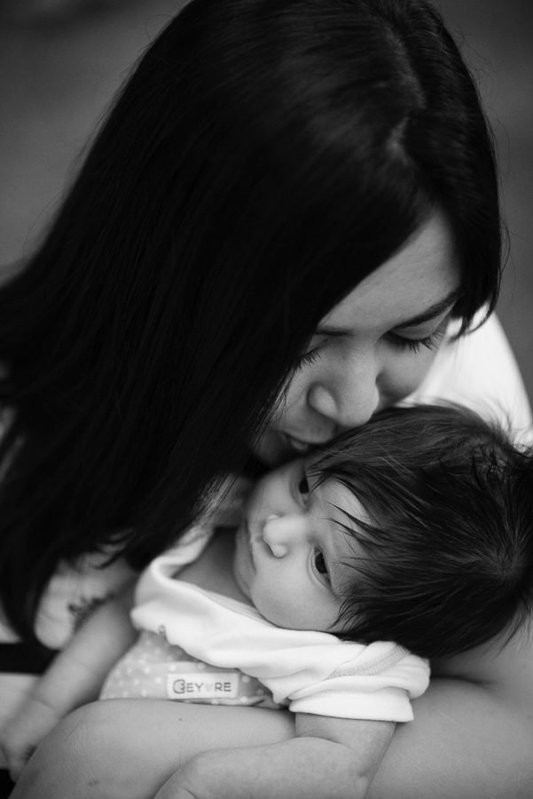 Black and white portrait of a mother kissing her newborn at a family celebration at home
