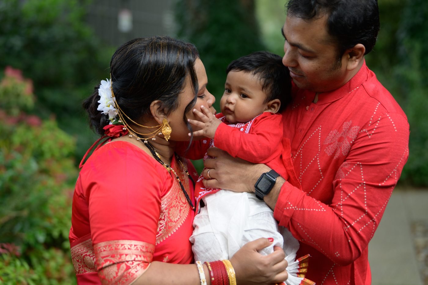 Parents holding their baby outdoors in traditional dress during a family celebration