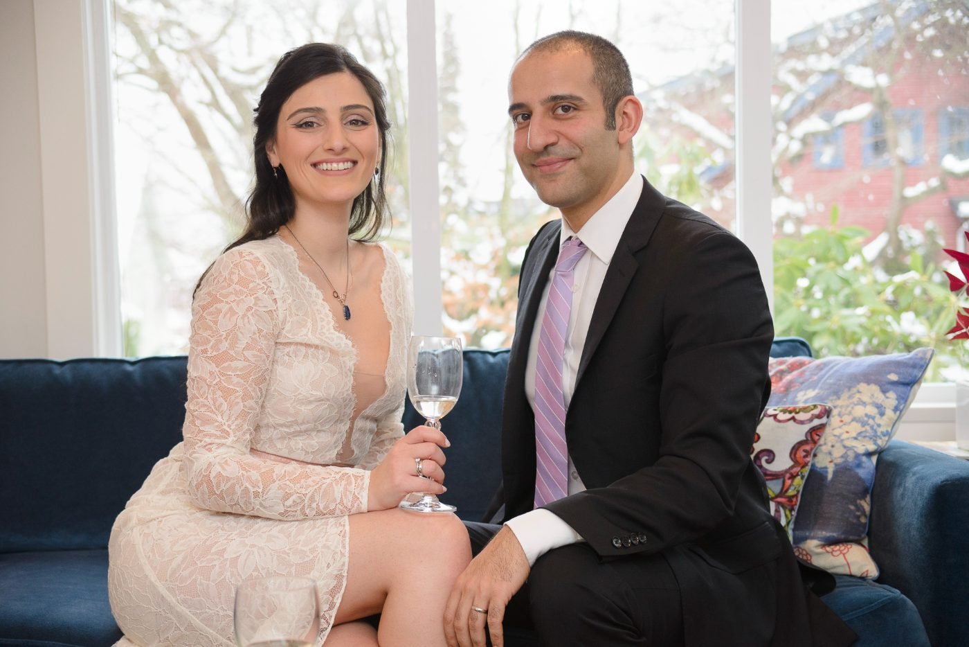 Newly married couple raising a glass indoors at their small winter wedding while snow falls outside the window