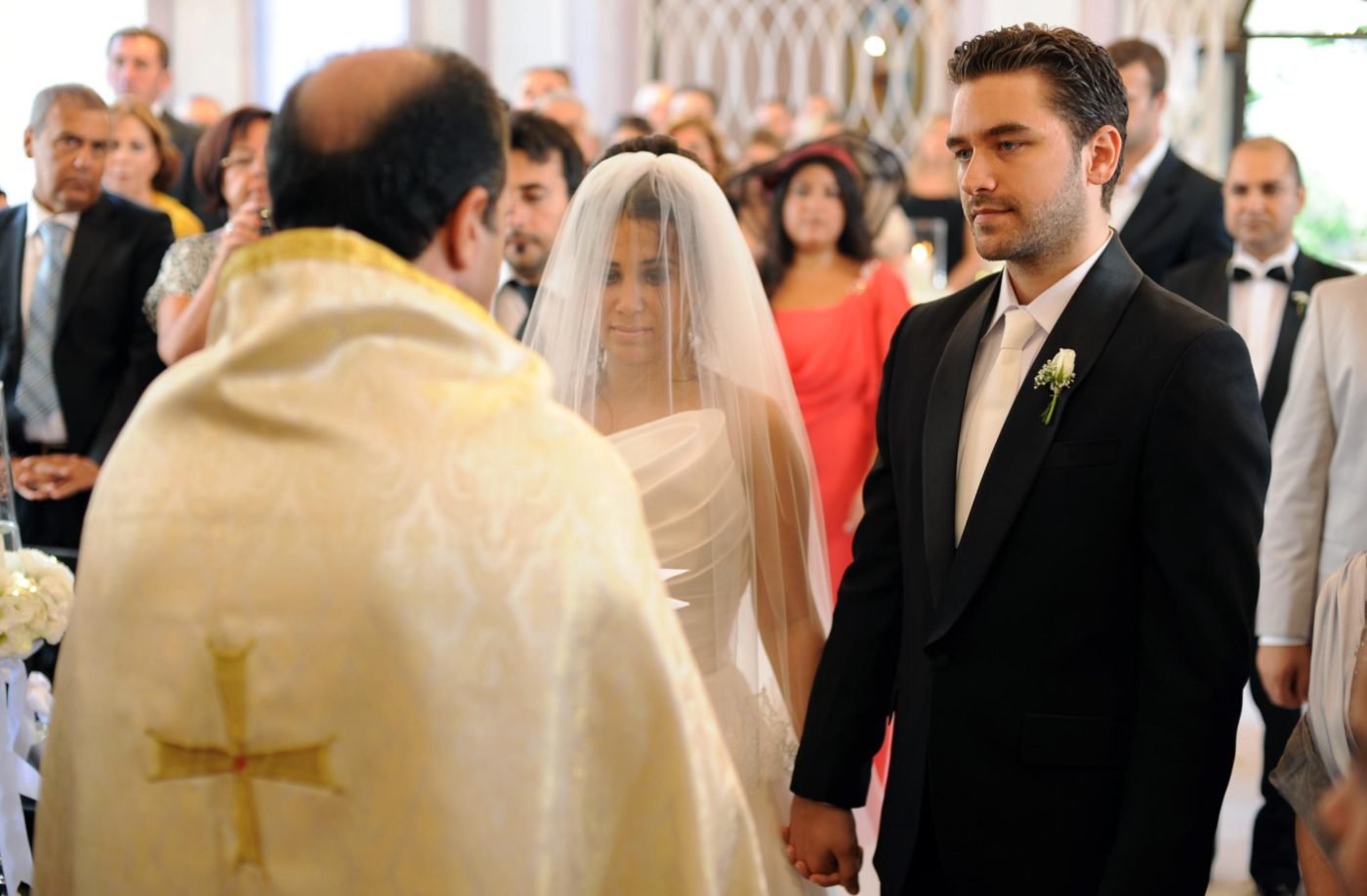 Wedding ceremony photography of a bride and groom holding hands in front of the priest during their church vows