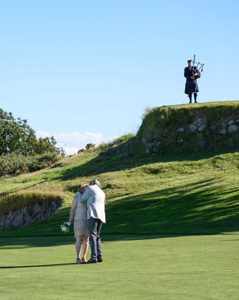 Newlyweds sharing a kiss on a wide green field under a clear blue sky