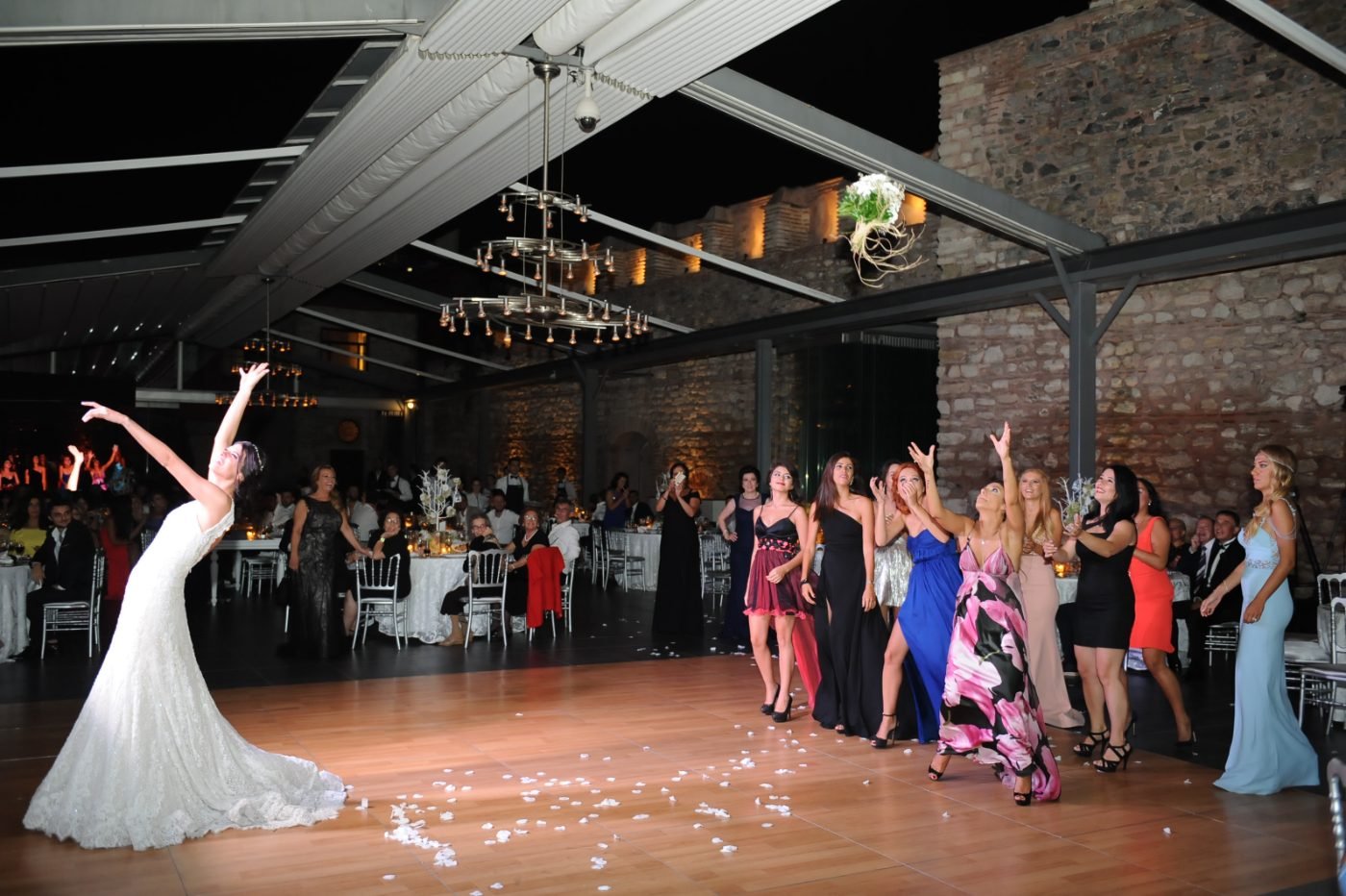 Wedding reception photography of the bride tossing her bouquet to guests waiting on the dance floor