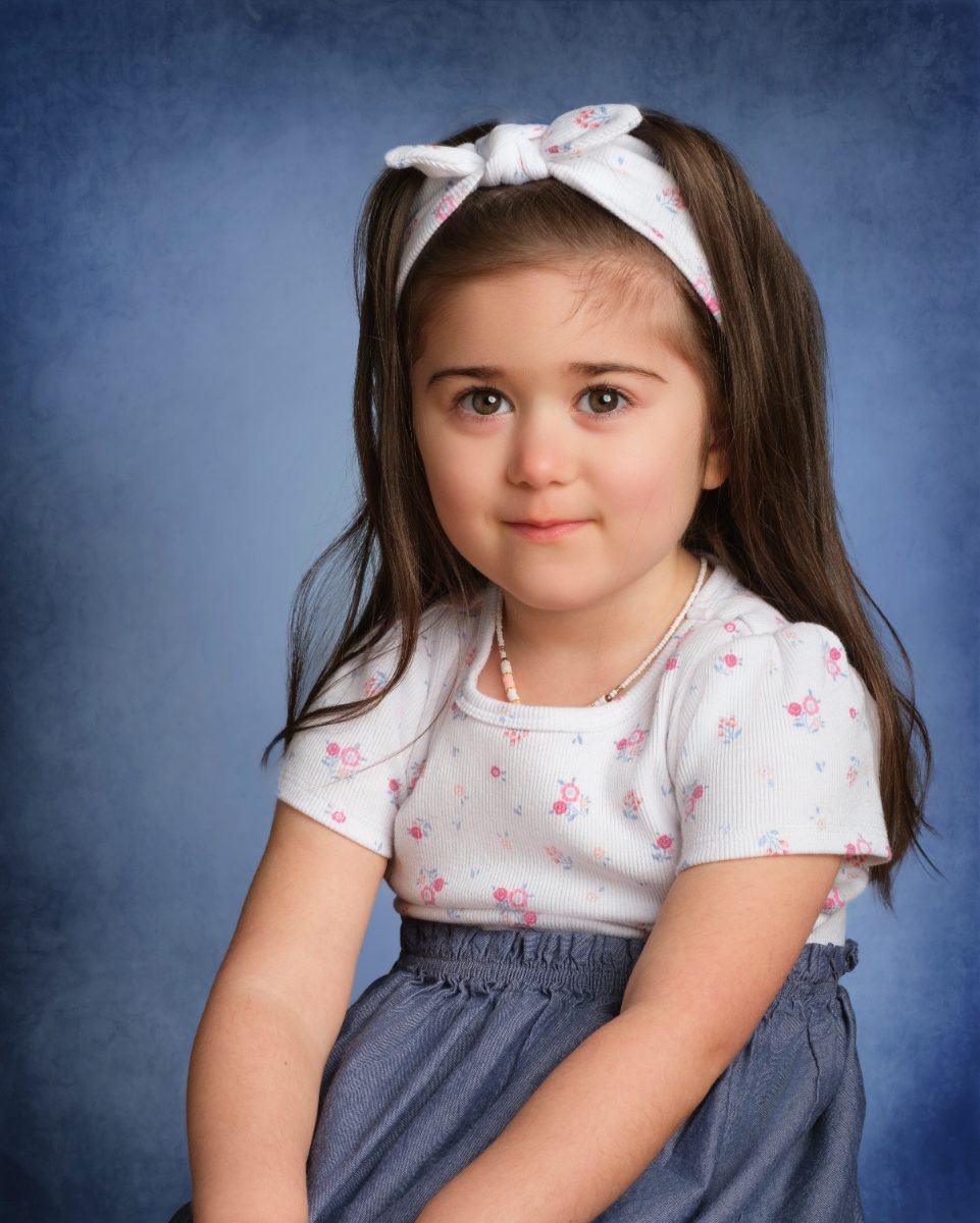 A girl with a white headband on a classic mottled blue school-photo backdrop