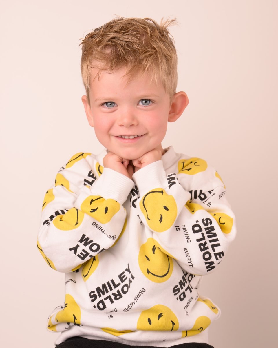 A boy in a smiley-face fleece top with his arms wrapped around himself