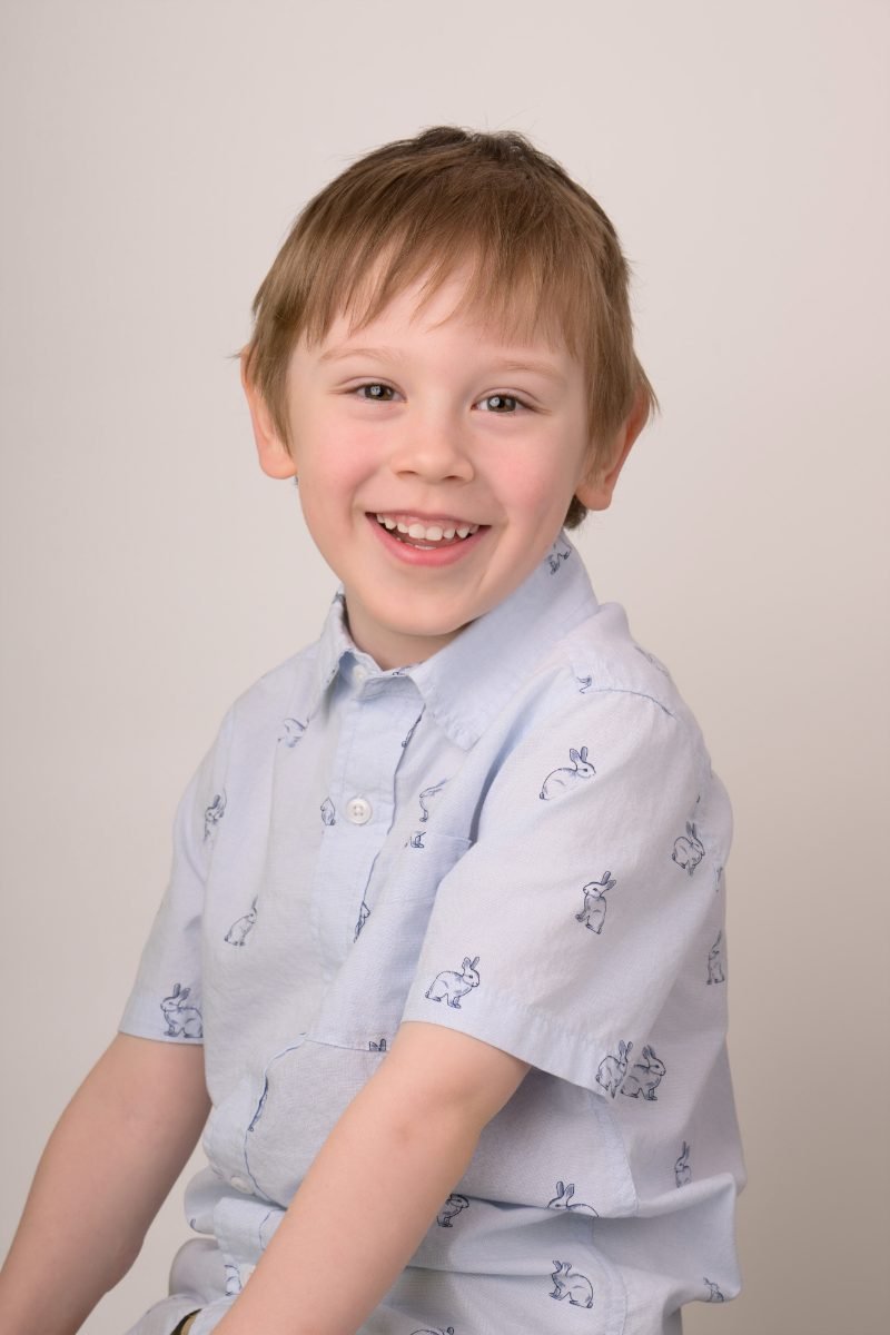 A boy in a pale blue patterned shirt with his shoulder turned to the camera