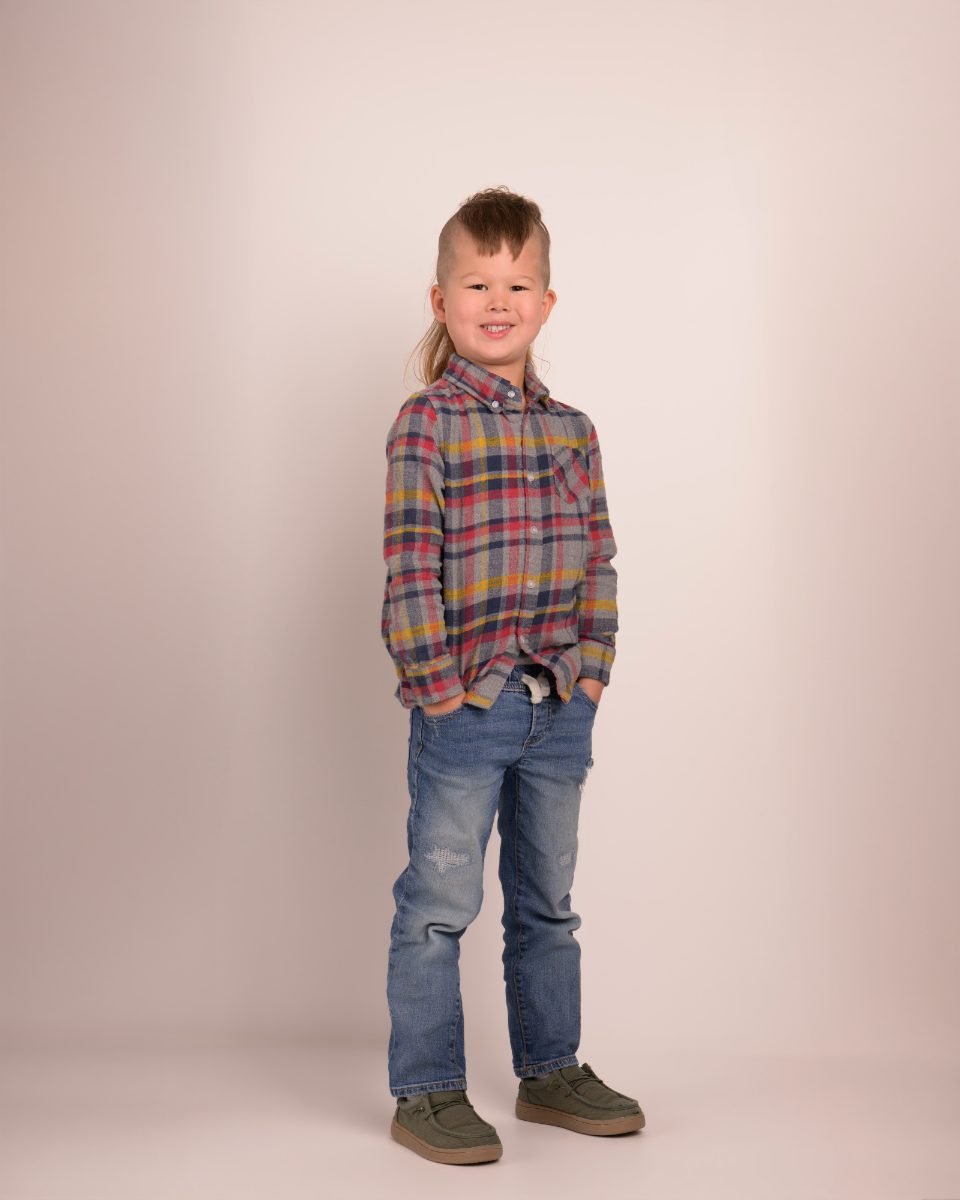 A boy in a plaid shirt and jeans photographed head to toe