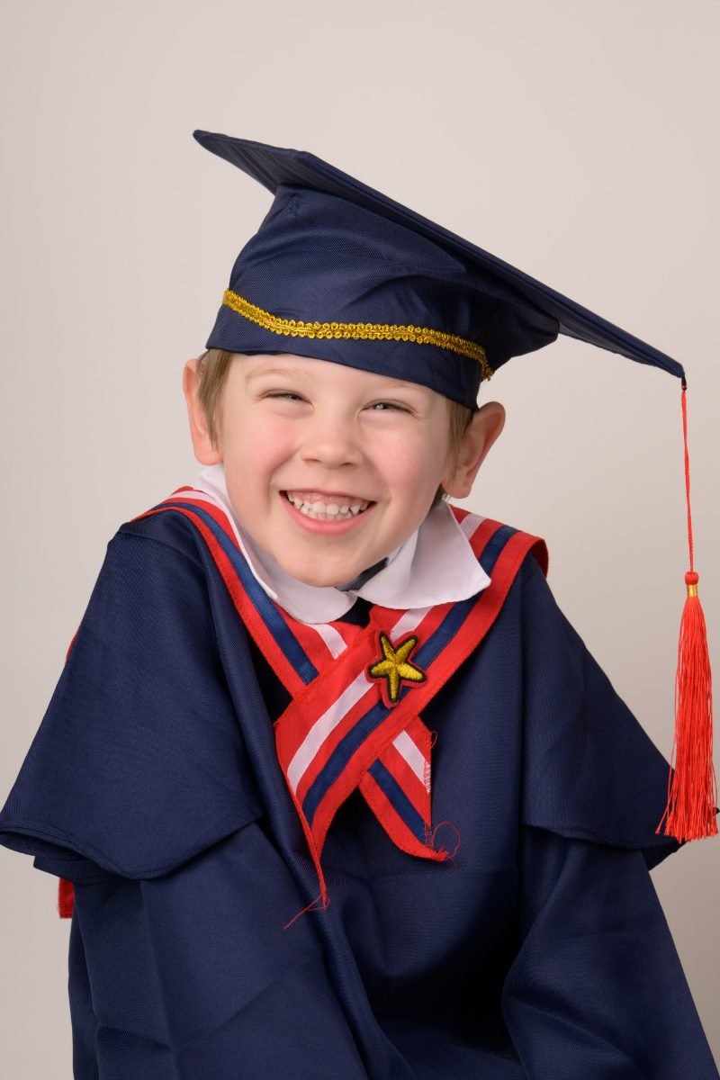 A preschool graduate laughing in a navy cap and gown with a red tassel