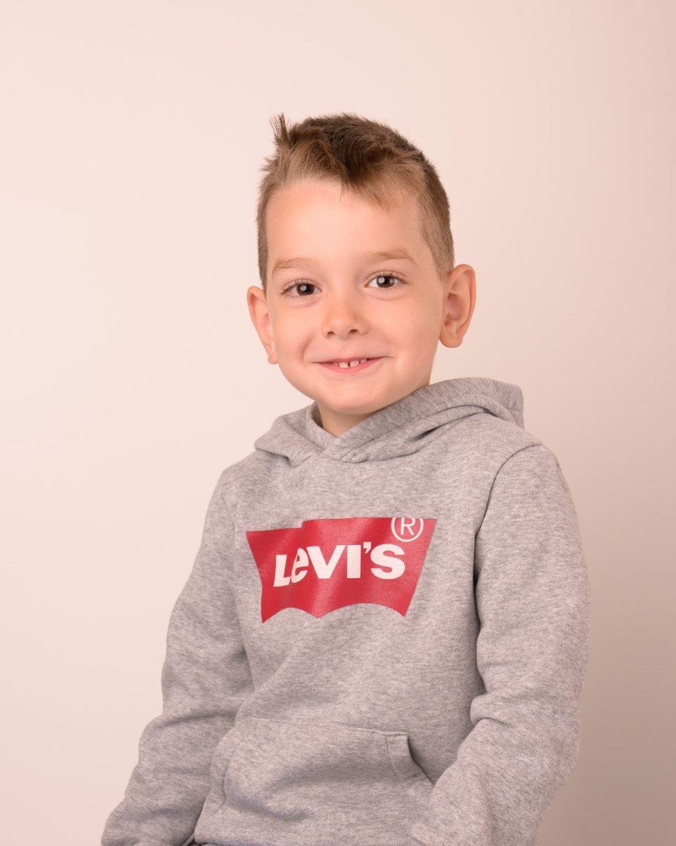 A boy in a grey hoodie smiling on a warm neutral backdrop