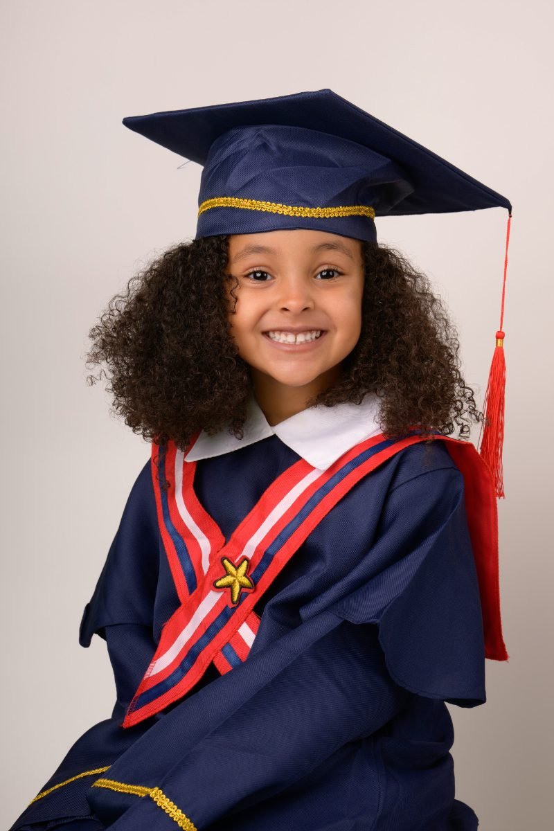 A preschool graduate with curly hair in a navy cap and gown