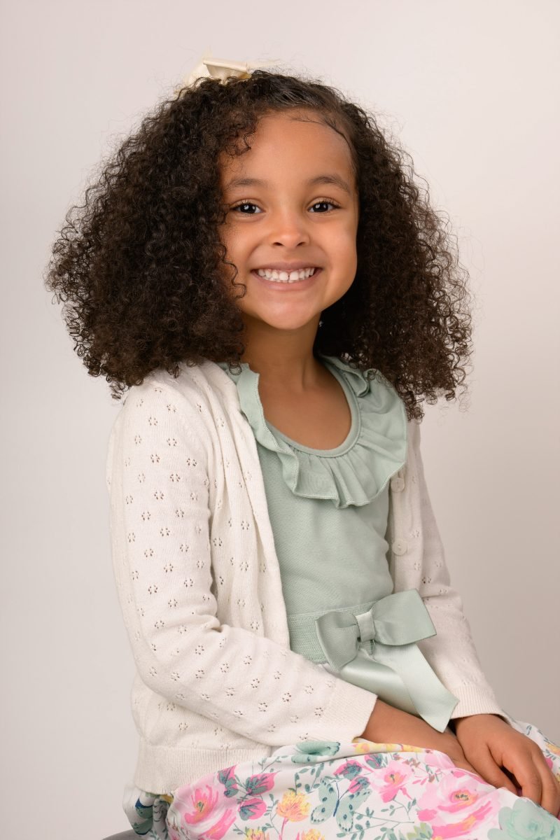 A girl with curly hair in a cream cardigan and sage top