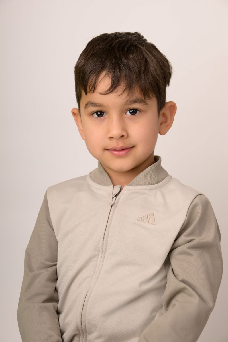 A boy in a tan zip-up top on a soft grey backdrop