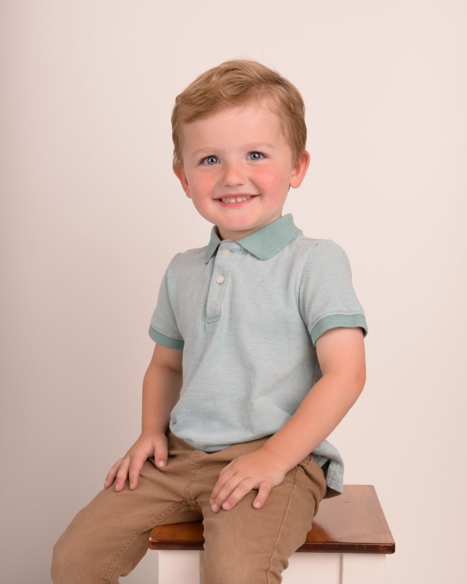 A boy in a mint polo sitting on a wooden stool