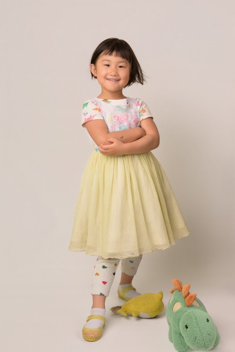 A girl in a yellow tulle skirt standing with her toy dinosaurs