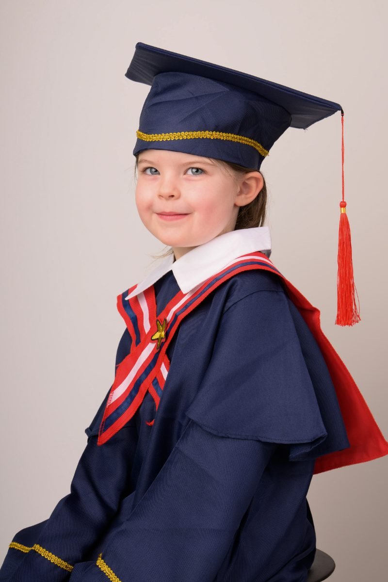 A preschool graduate in a navy cap and gown with a red-lined hood