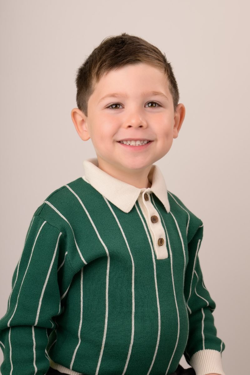 A boy in a green striped polo sweater smiling at the camera