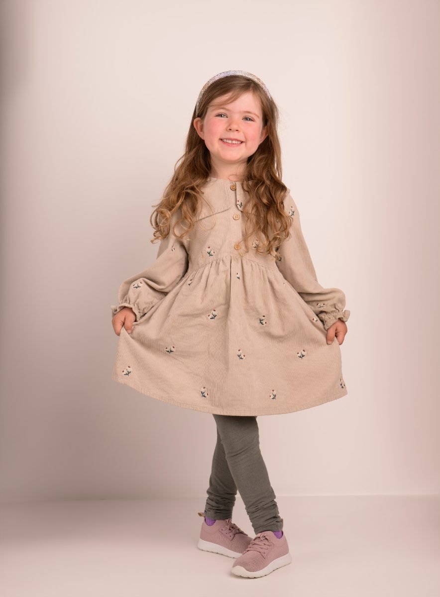 A girl in a beige dress photographed head to toe, skirt swinging