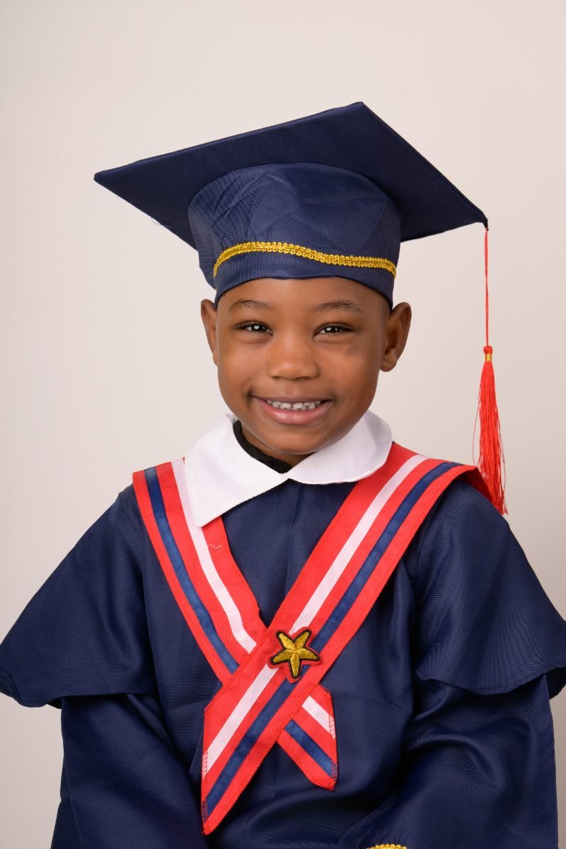 A preschool graduate in a navy cap and gown with a red and white stole