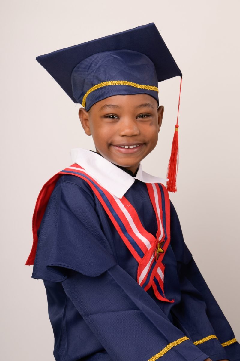 A preschool graduate in a navy cap and gown with a red and white stole