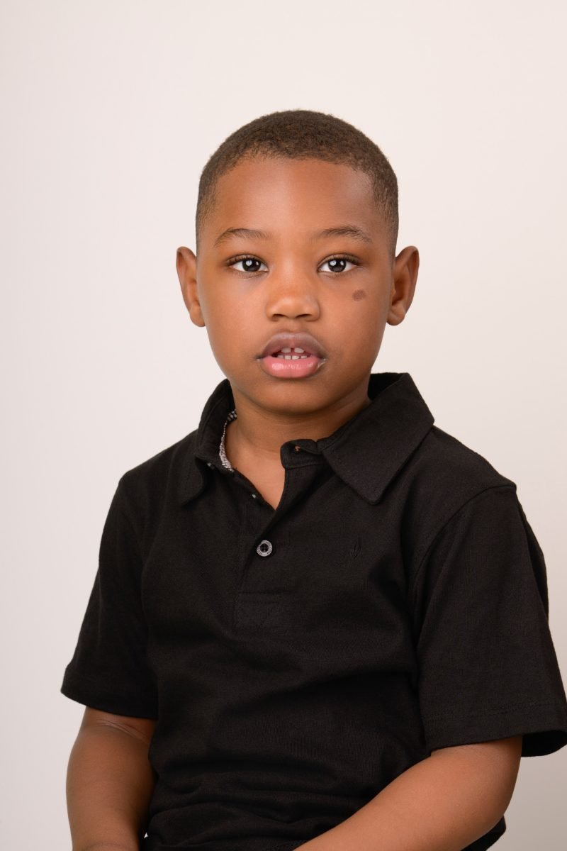 A boy in a black polo shirt on a warm neutral backdrop