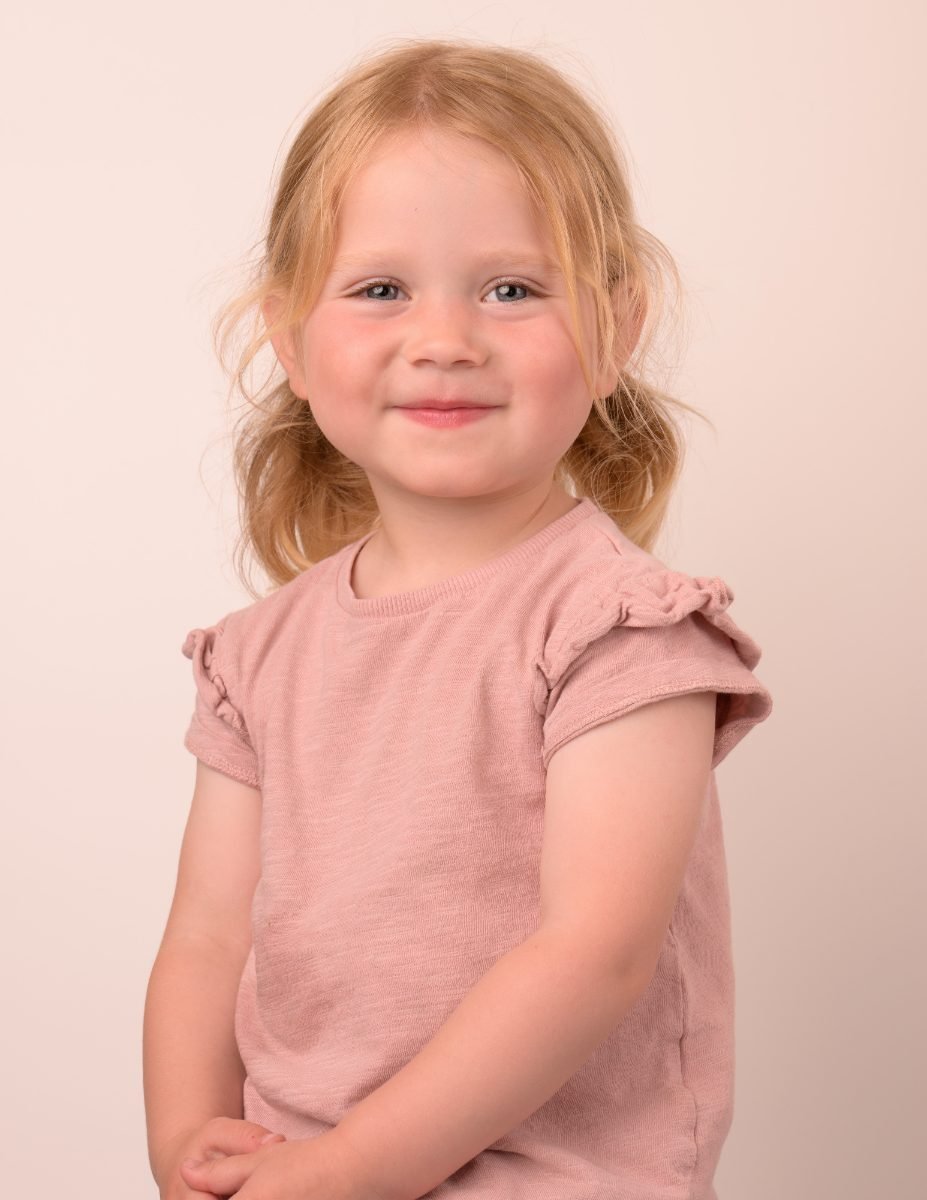 A girl in a dusty pink ruffle top smiling softly