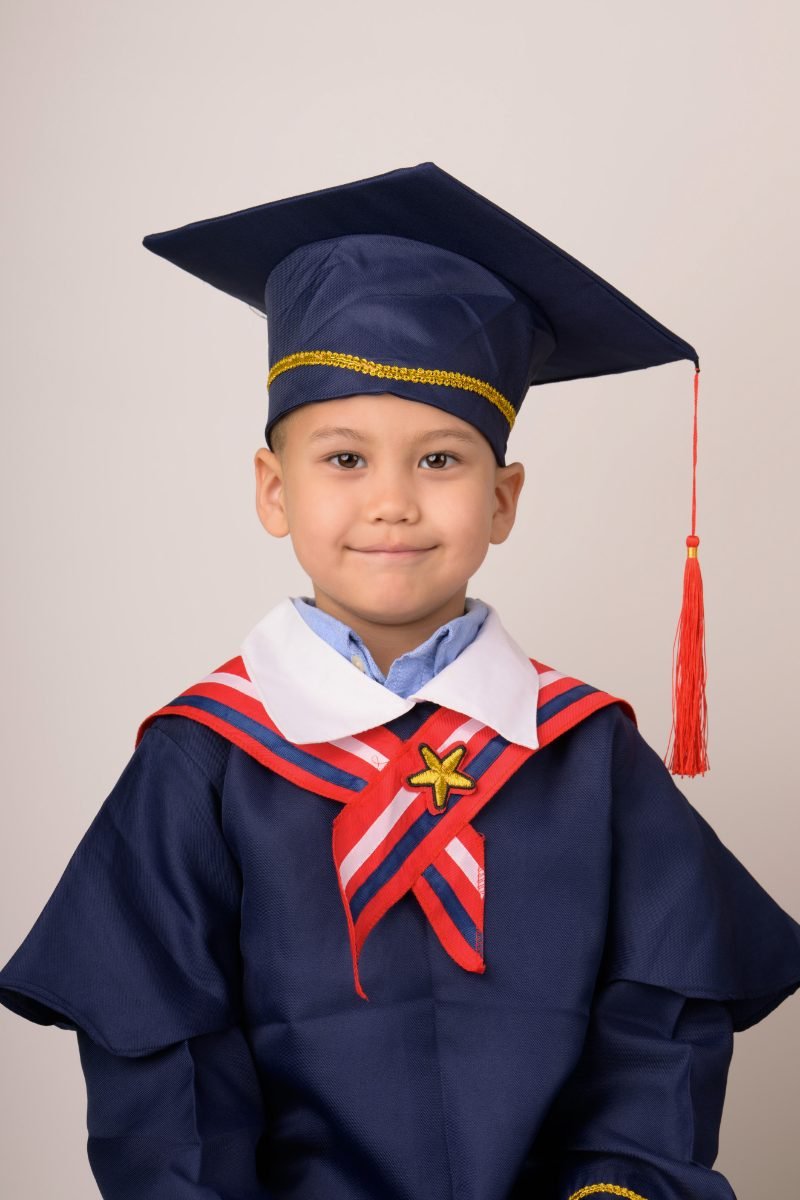 A preschool graduate in a navy cap and gown with his hands folded