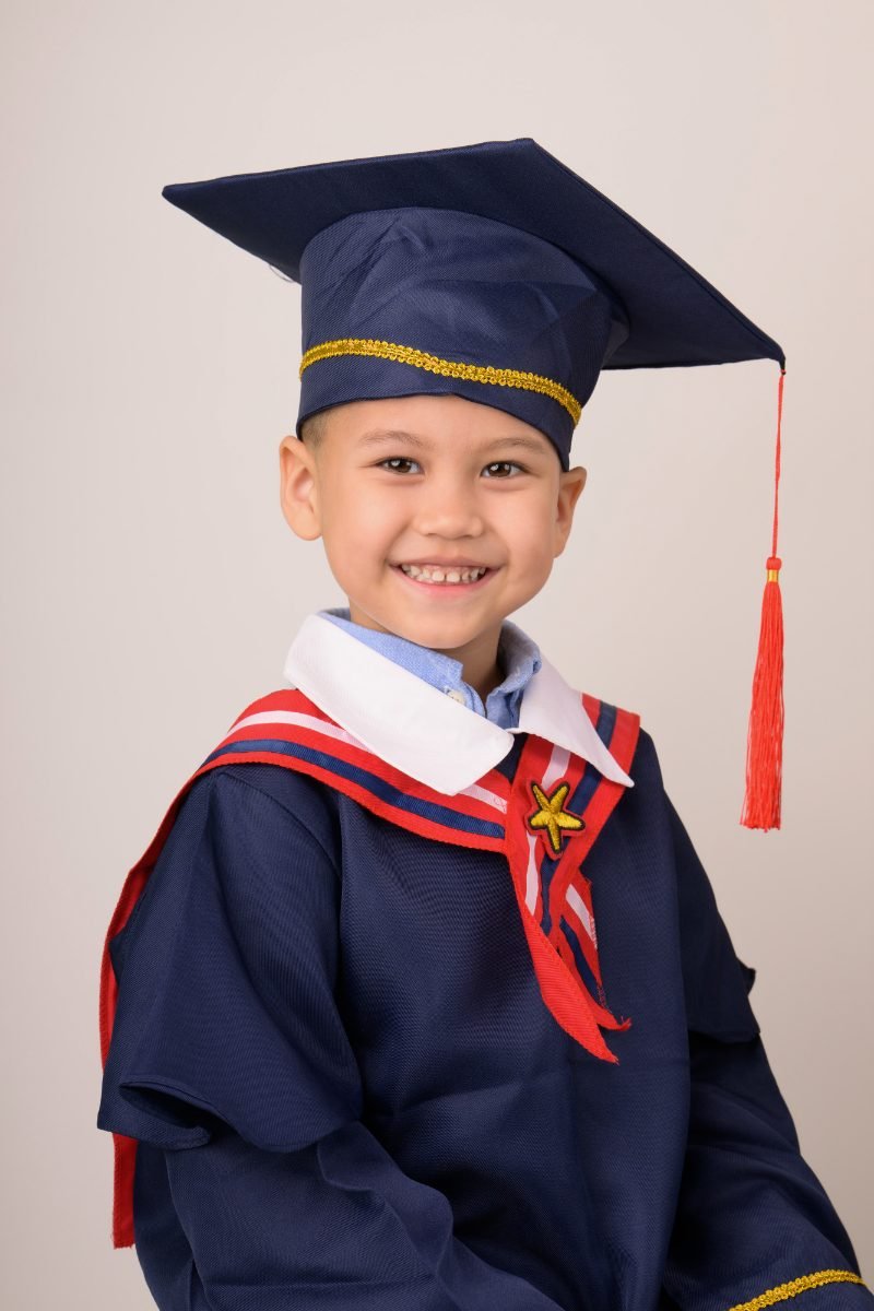 A preschool graduate in a navy cap and gown with his chin lifted